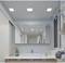 Modern bathroom with a large mirror, washbasin, plant in a glass vessel and towel on a hook. Ceiling lights illuminate the room.