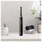 A black electric toothbrush stands upright on a bathroom counter with rolled towels, a soap dispenser, and white orchids in the background.