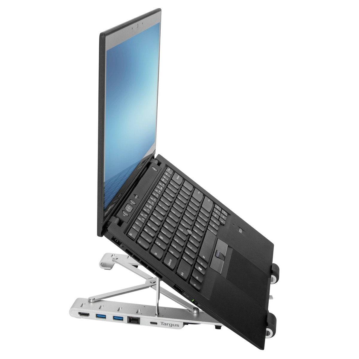A laptop sits on an adjustable-height stand, which improves tilt and air circulation. The screen displays a blue background.