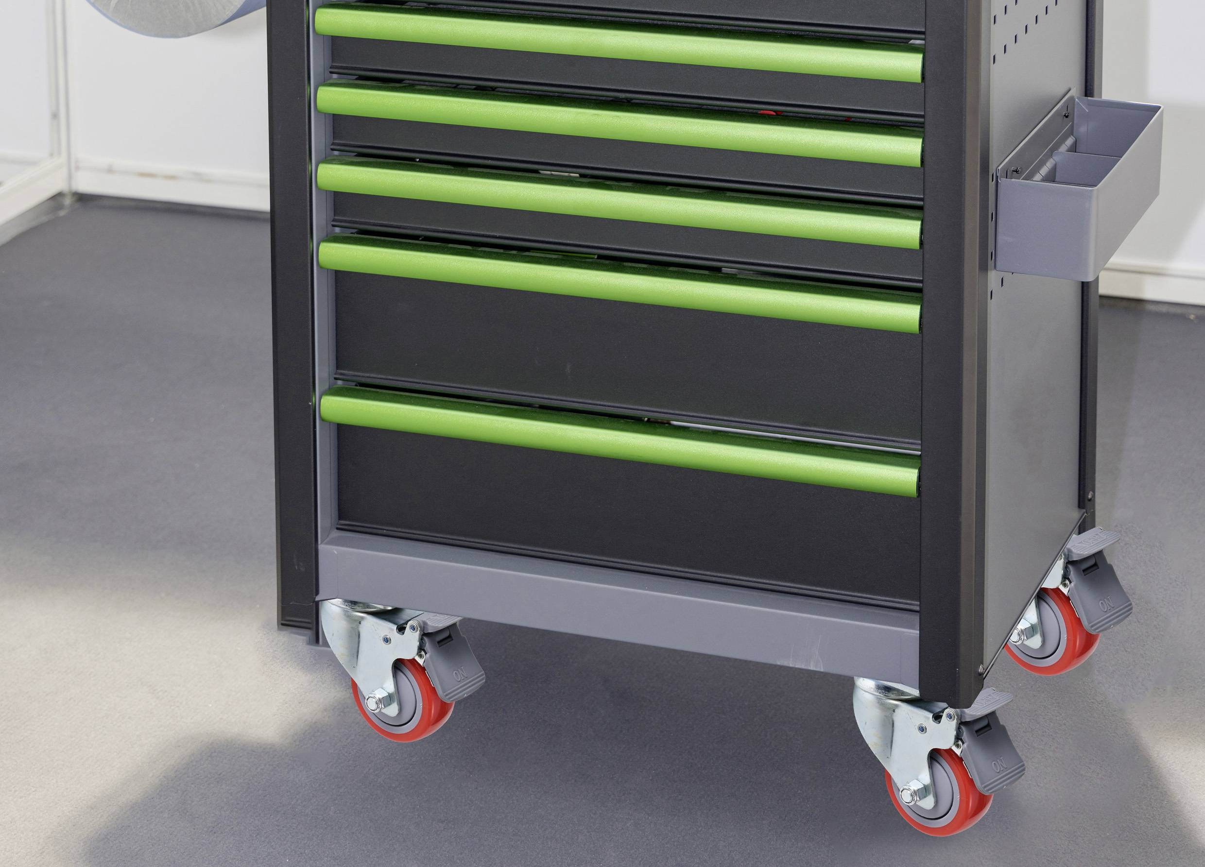 Toolbox on wheels with five green handles on the drawers, standing on a grey floor.