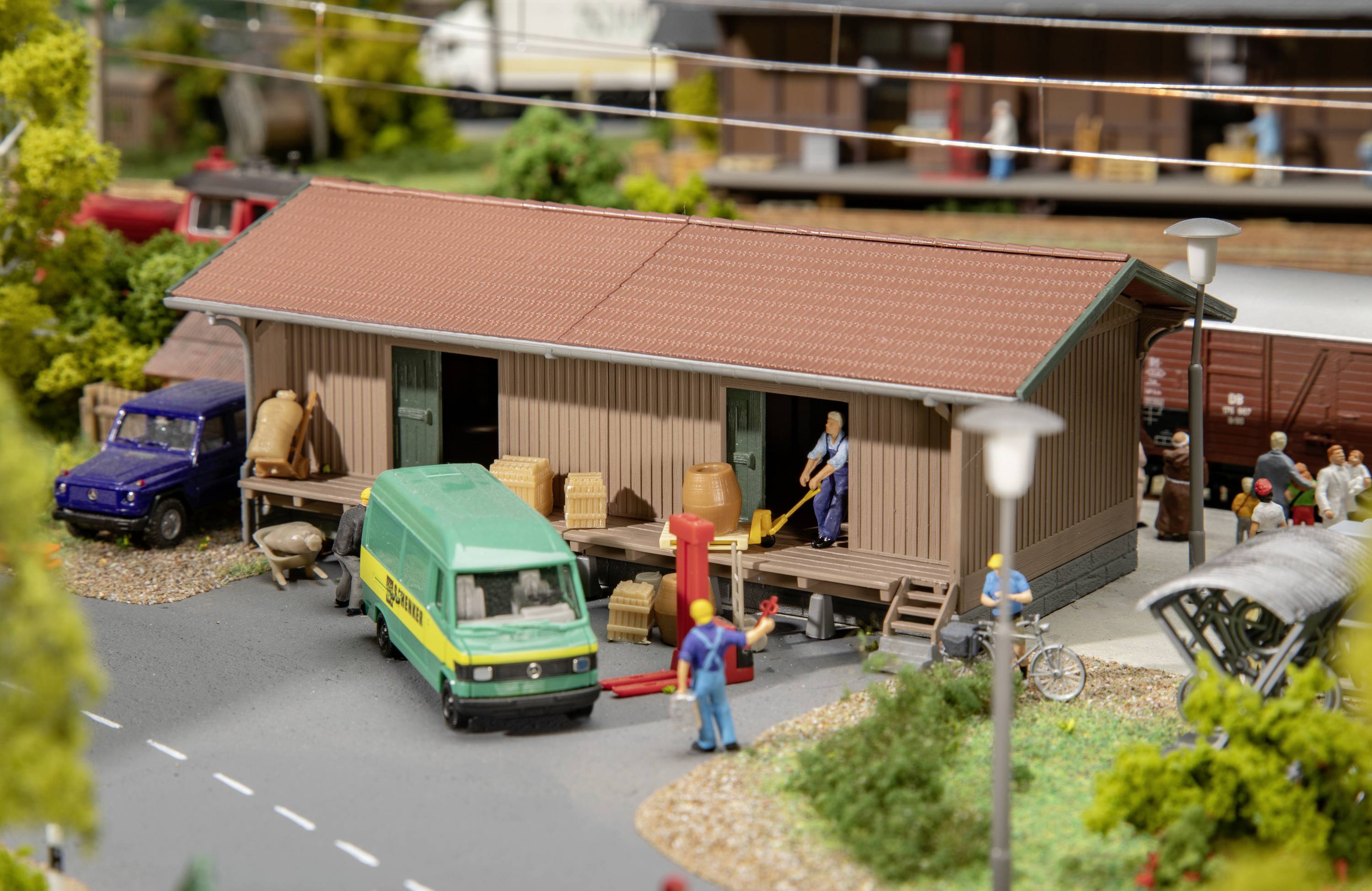 Miniature model of a logistics centre featuring vehicles, figurines working, and a green delivery van in front of a warehouse.