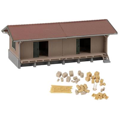 A model of a warehouse with a red roof. In the foreground are several small model-building elements such as crates, barrels, and sacks.