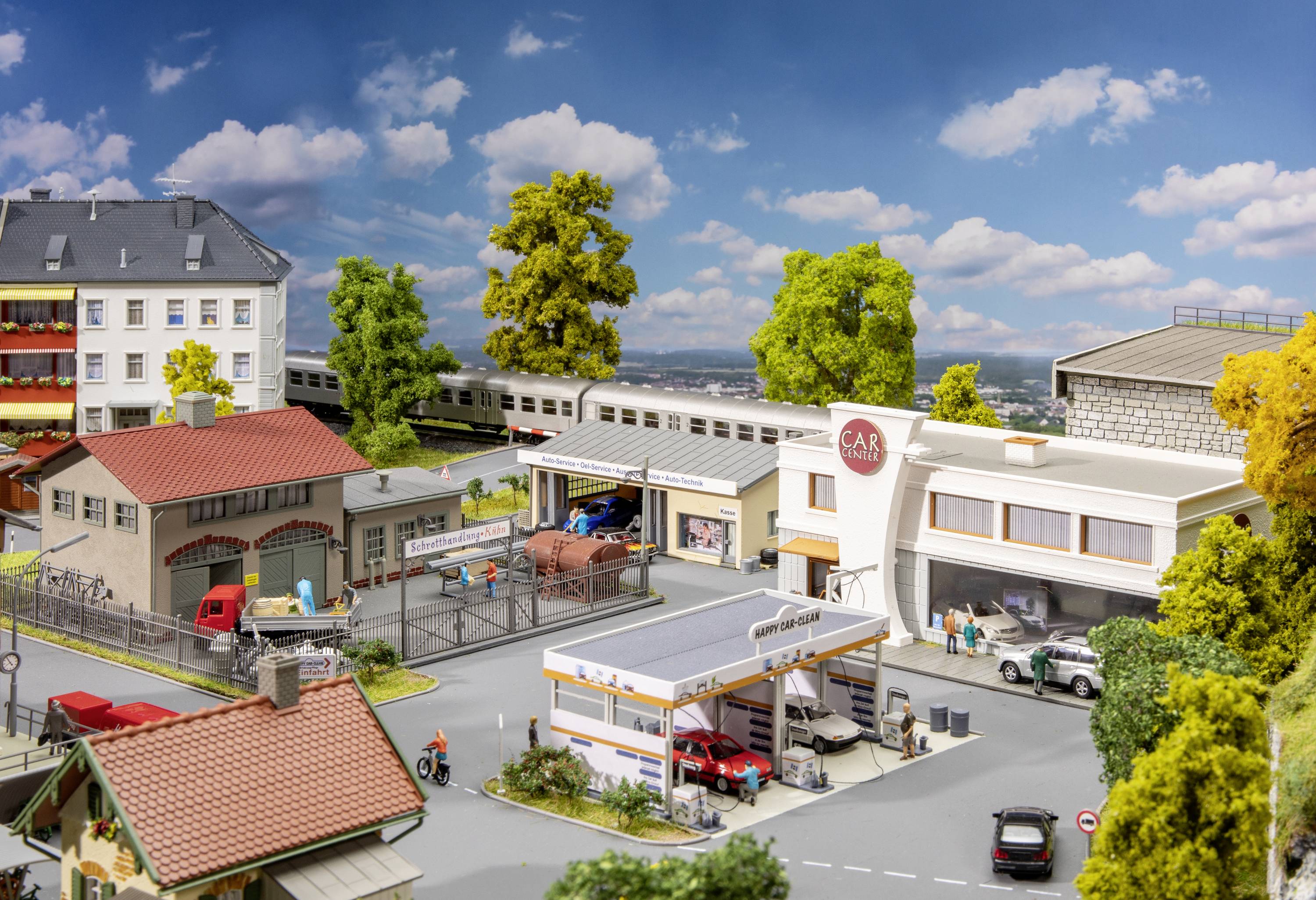 A miniature town shows a petrol station, a car repair workshop and residential houses. Trees and a train in the background complement the scene.