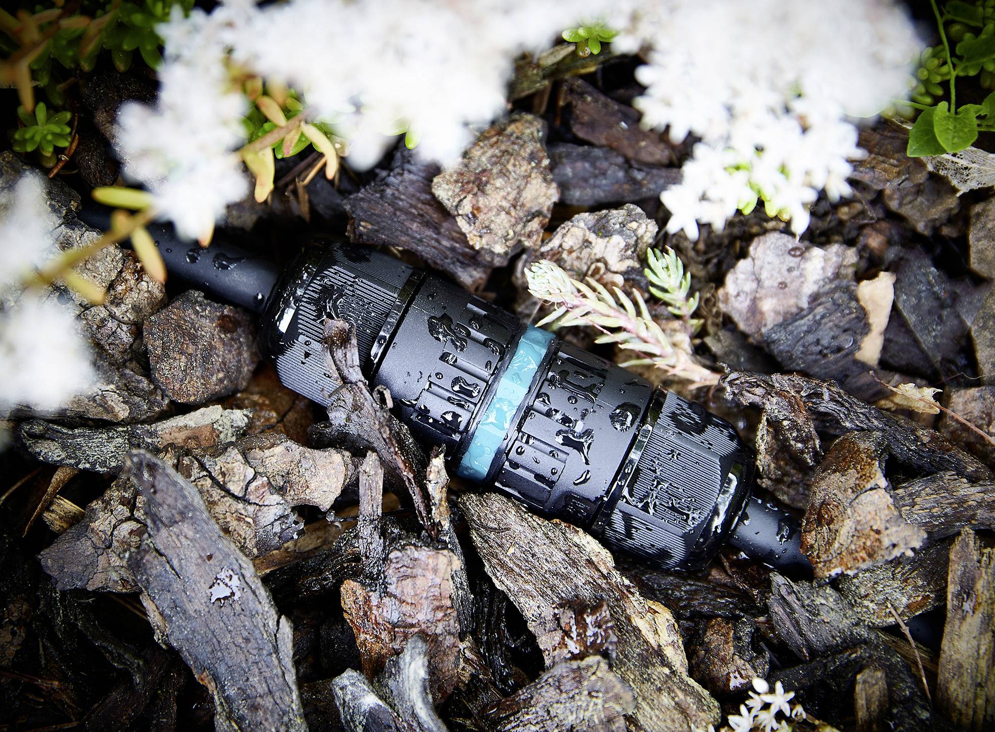 A black, water-resistant cable connector lies on wet wood, surrounded by white blossoms.