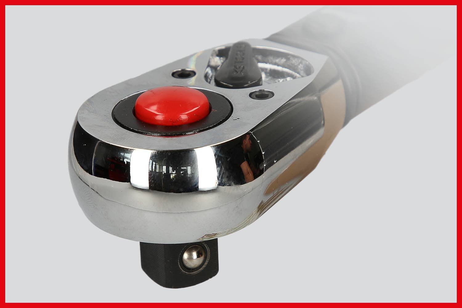 Ratchet with a red button in close-up on a grey background. Shiny metallic surface with visible working mechanism.
