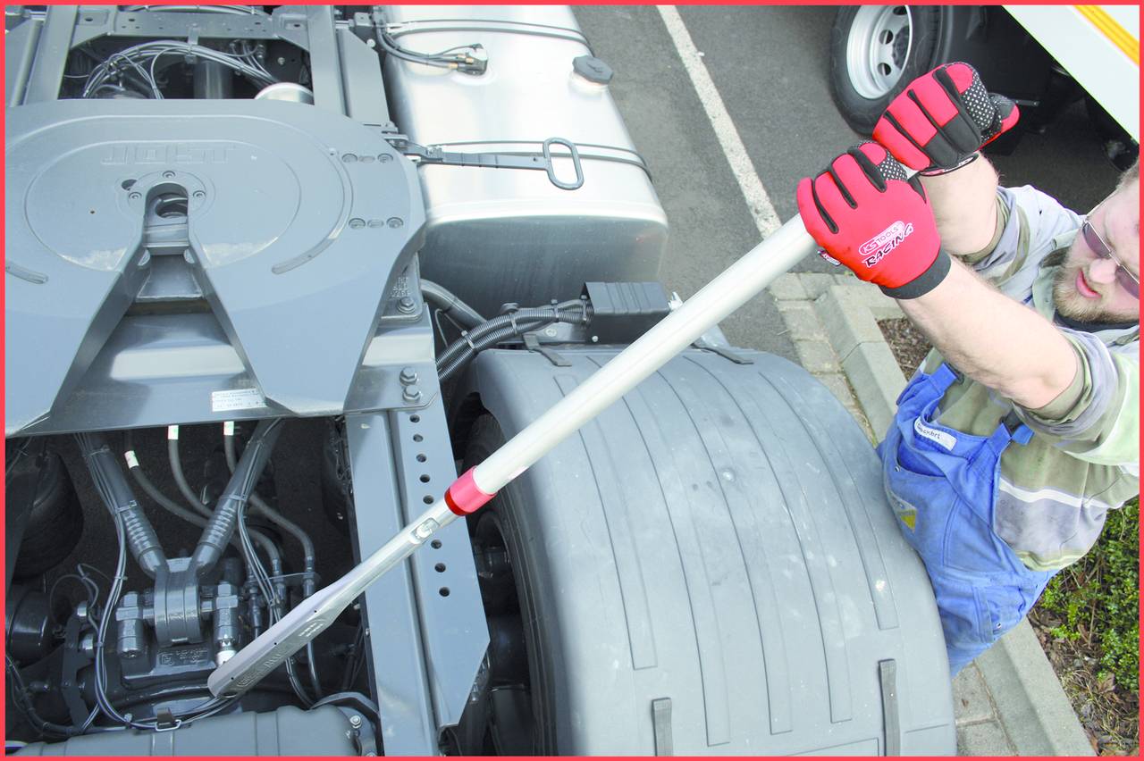 A mechanic wearing red gloves pulls a lever on a lorry chassis to carry out mechanical maintenance work.