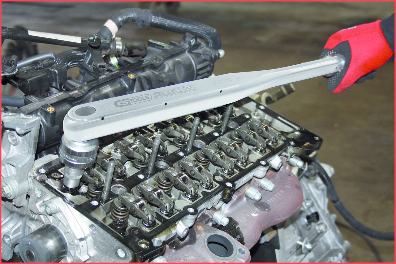 A mechanic tightens bolts on the engine block using a torque wrench; demonstrating precise work on an exposed engine.