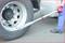 A person is using a torque wrench to tighten a lorry wheel. The tool is positioned on a wheel nut, with a road in the background.