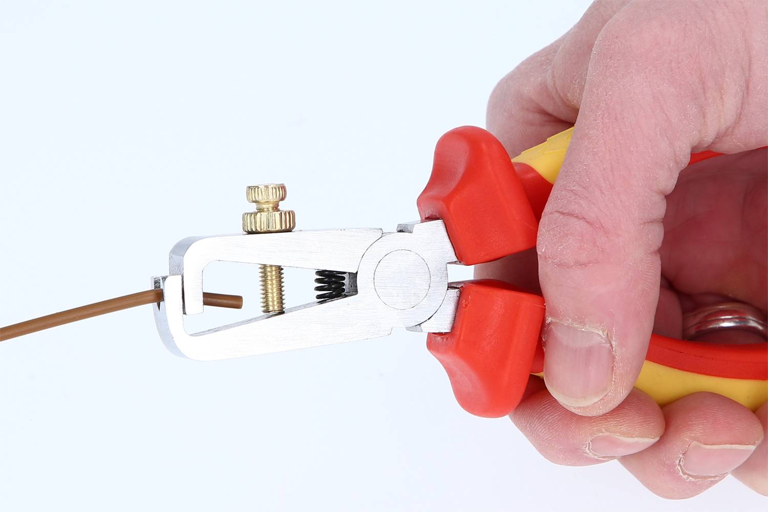 A hand is holding a wire stripping plier, stripping the insulation from a brown cable.