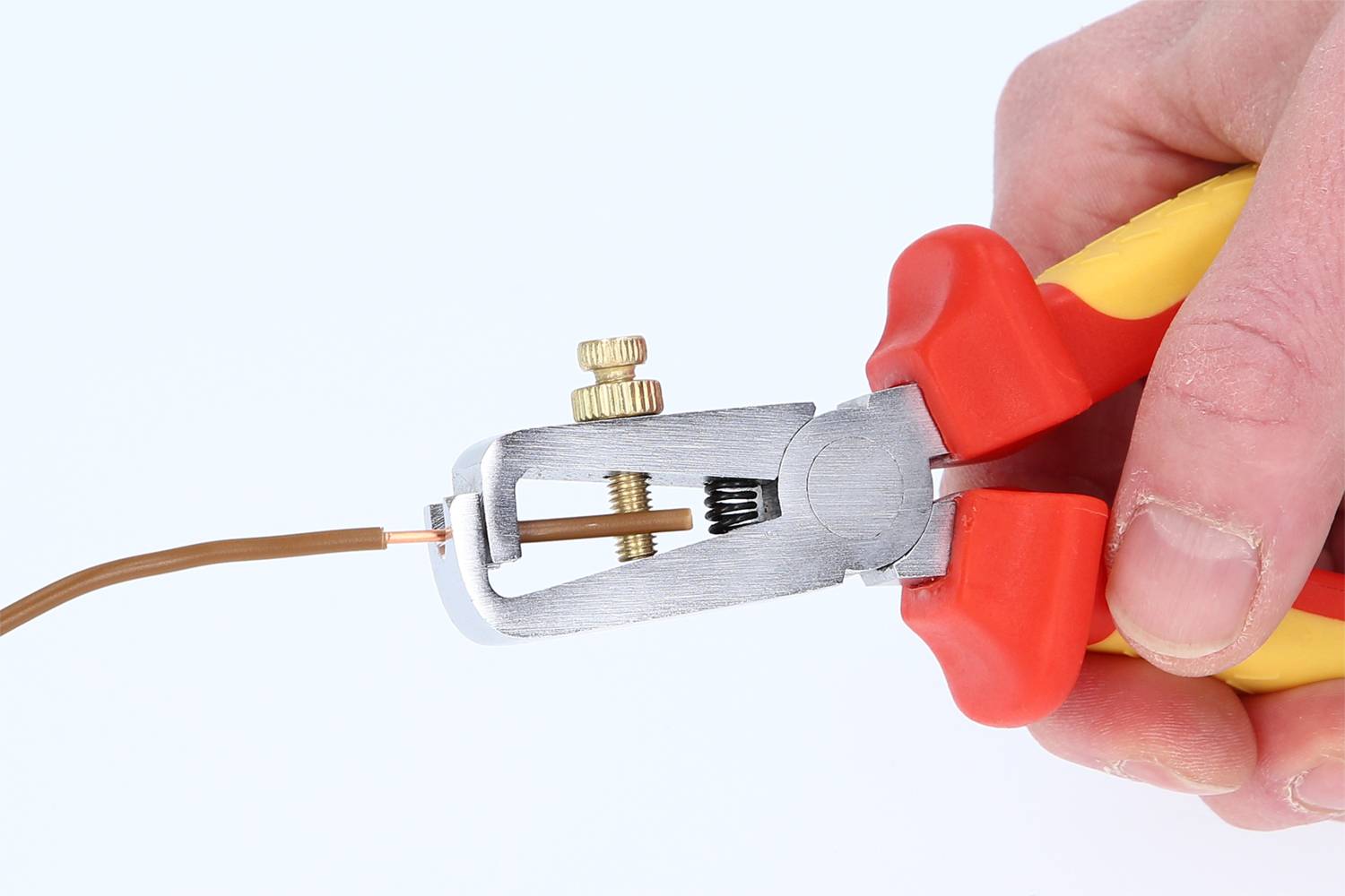 A hand holds red and yellow wire strippers, which are stripping a brown cable.