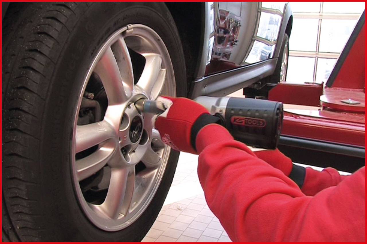 A person is tightening the wheel nuts of a car with an electric impact wrench. The car is located on a vehicle lift.
