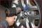 A hand positions an impact driver onto a wheel nut on a BMW car to loosen or tighten the wheel bolts.