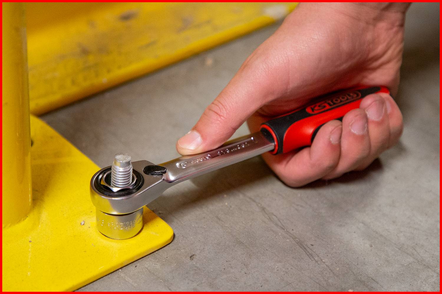 A hand is using a socket spanner to tighten a screw on a yellow metal structure.