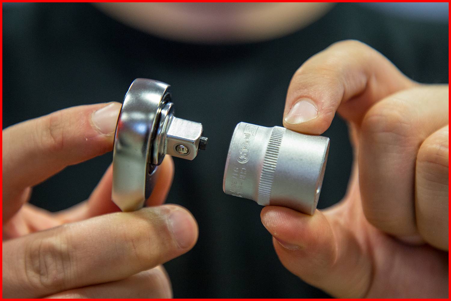 A person is holding a ratchet and a socket which are being fitted together at that moment.
