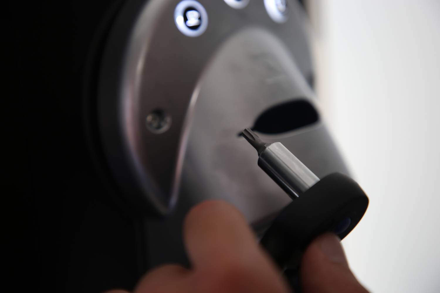 A hand holds an electronic device in front of a lock with illuminated symbols, possibly a security access device.