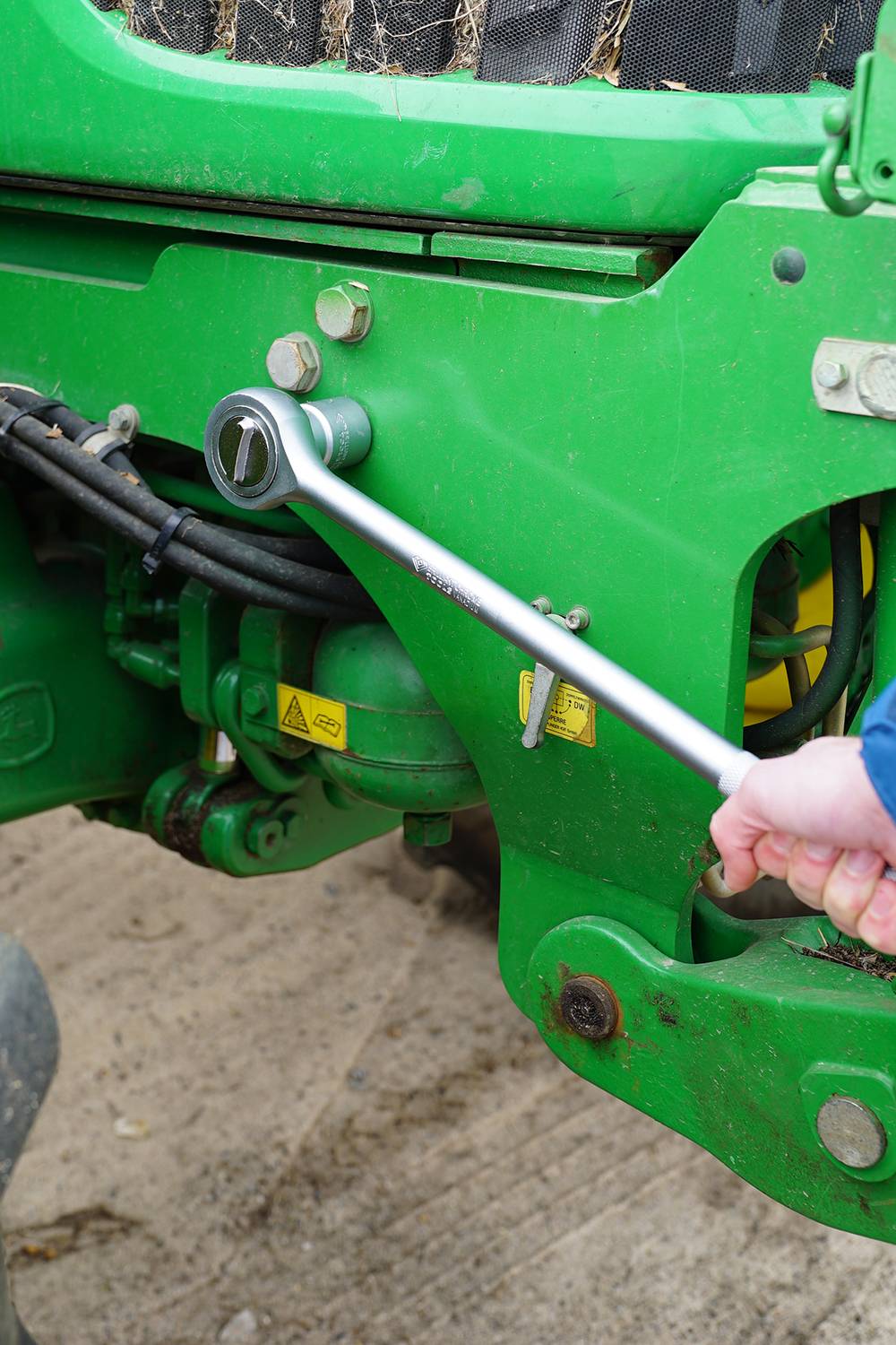 A person is tightening a spanner on green agricultural equipment. Screws are being secured at the front of the device.