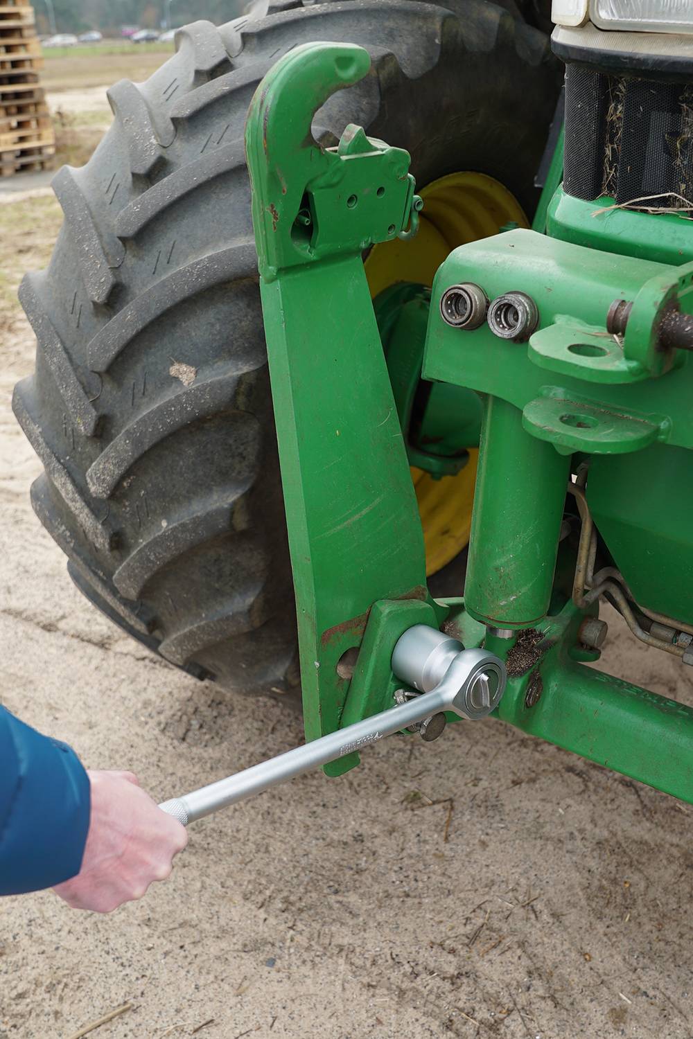 A person is using a spanner to repair a green agricultural machine.