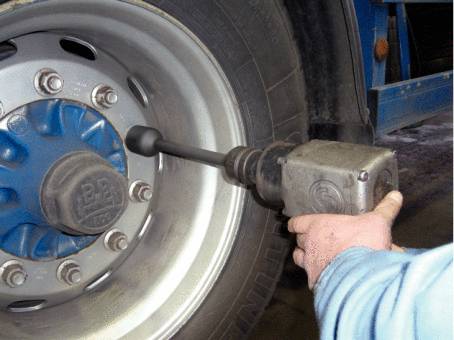 A person is tightening the wheel nuts of a lorry tyre using an electric impact wrench.