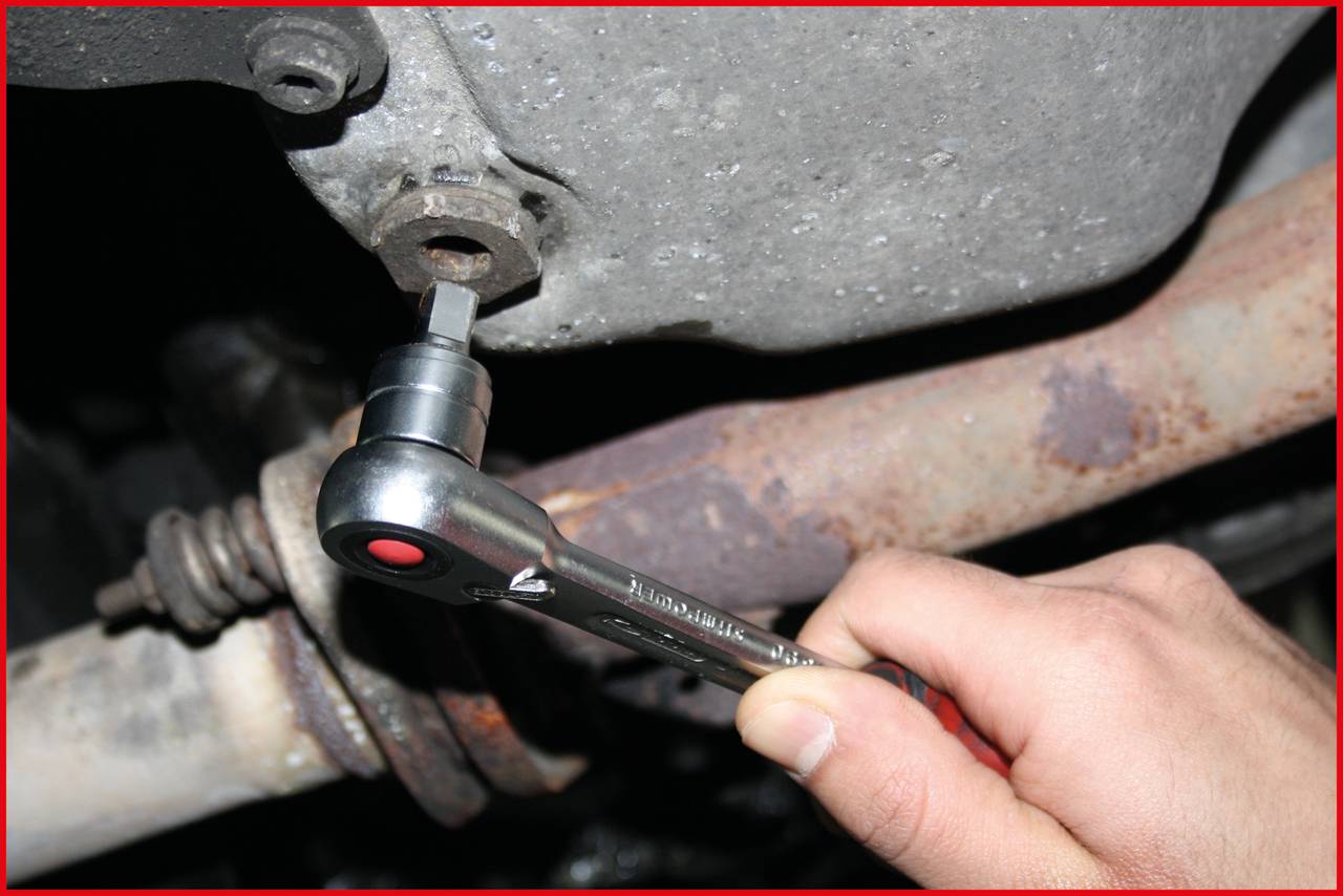 Someone is repairing a car with a socket spanner in close-up. Tool gripping a screw underneath a vehicle.