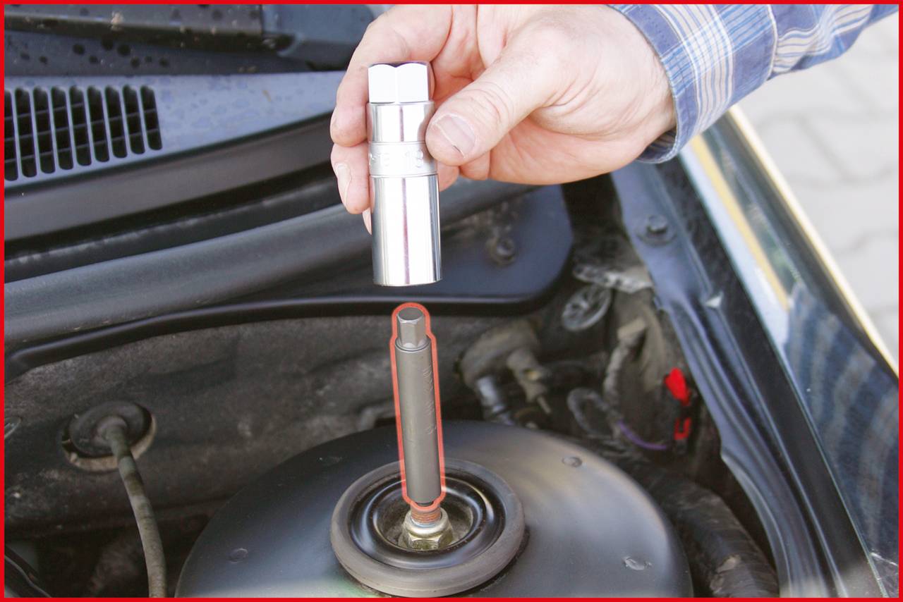 A hand is holding a spanner over a nut on a shock absorber in a car's engine bay.