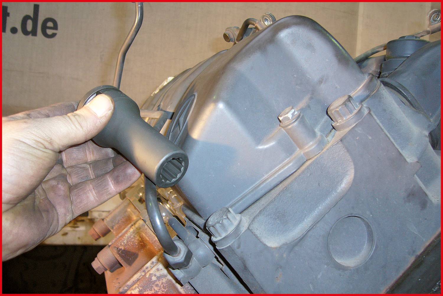 A hand is holding a specialised tool that is being placed onto a bolt of a grey-painted machine or motor component.