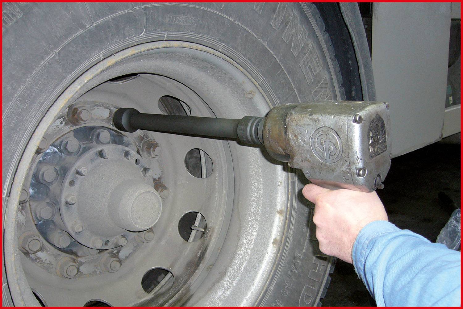 A person is using a pneumatic impact wrench to secure the wheel nuts of a large vehicle tyre.