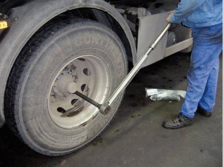 A person is changing a lorry tyre using a torque wrench. Scenario: Workshop environment, focused on practical work.