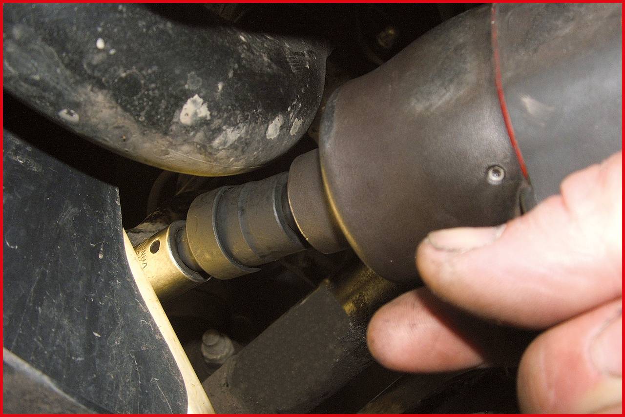 Close-up of a hand using an electric tool to secure a screw to a metal component. Environment shows vehicle parts.