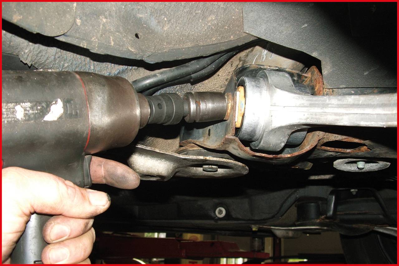 A person is using an electric drill to secure an automotive part underneath the vehicle.