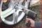 A hand is using an impact driver to tighten the wheel nuts of a car tyre with a silver rim.