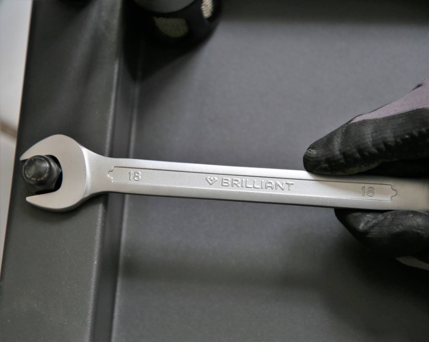 A spanner with 'Brilliant' engraved, is held by a gloved hand and positioned against a screw.