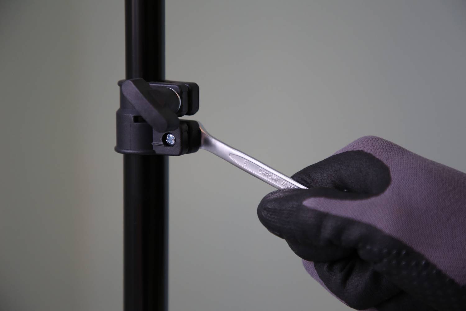 A gloved hand tightens a screw on a black stand using a spanner.