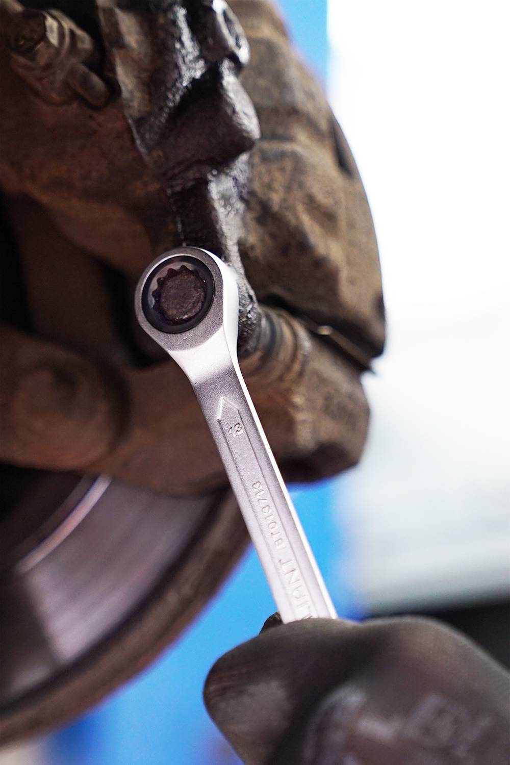 A hand wearing a glove grips a spanner and is working on a vehicle brake, focusing on repair.