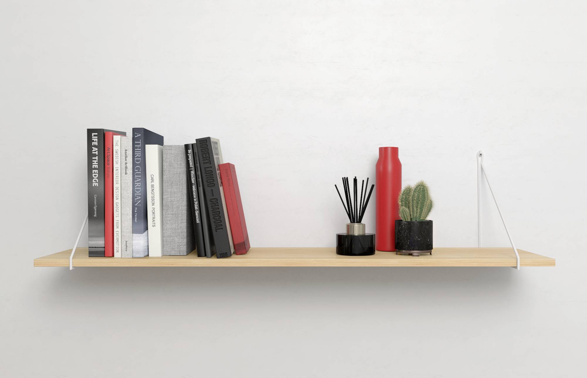 A wooden shelving unit against a wall displaying books, a diffuser, a red bottle, and a small cactus.
