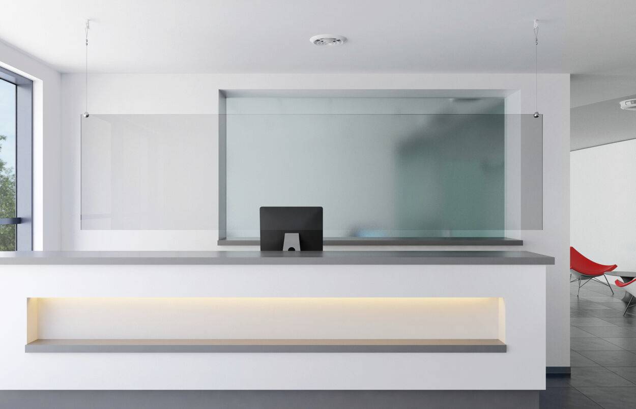 Modern reception area with a desk, a computer monitor and a Perspex partition; rectangular architecture.