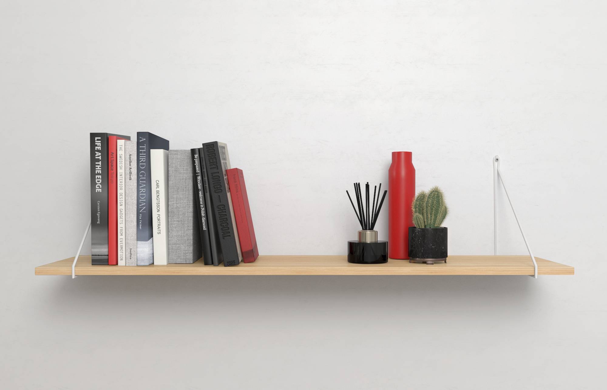 A wooden shelf with books, a red thermos, a small cactus, and a black reed diffuser against a white wall.