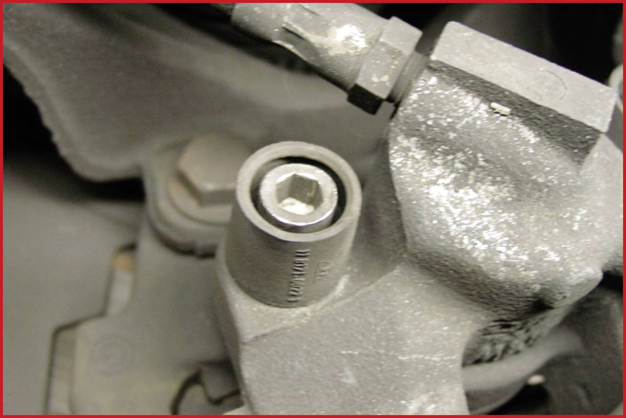 Close-up of a dirty hexagonal bolt in a mechanical device. The surrounding area shows worn metal components.