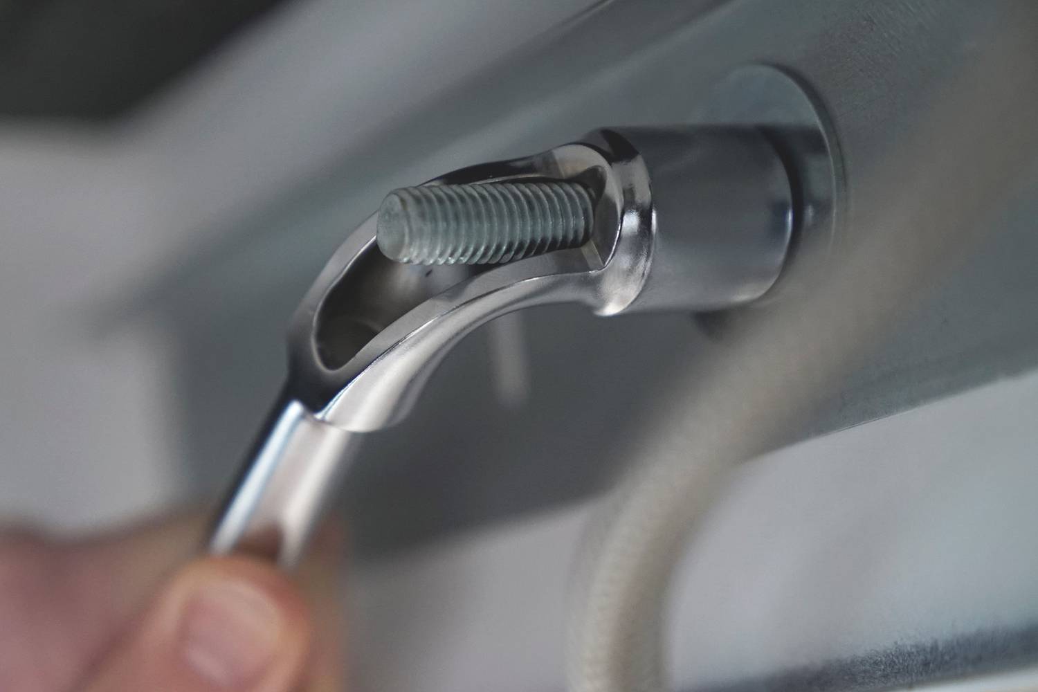 Close-up of an adjustable spanner turning a screw into metal. A hand is gripping the tool.