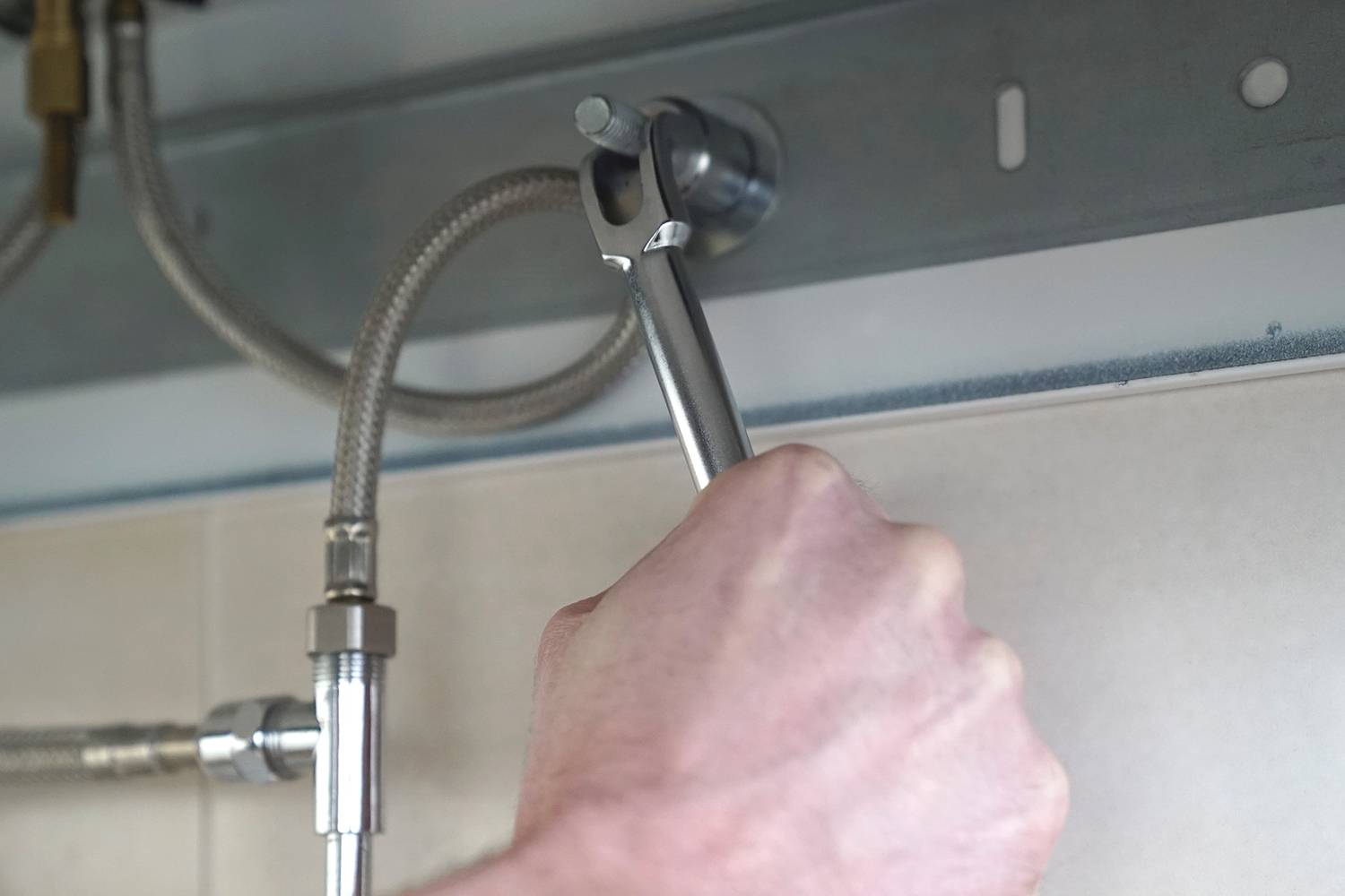 'A tradesman pulls on a spanner to tighten a large nut, securing a metal pipe beneath a sink.'