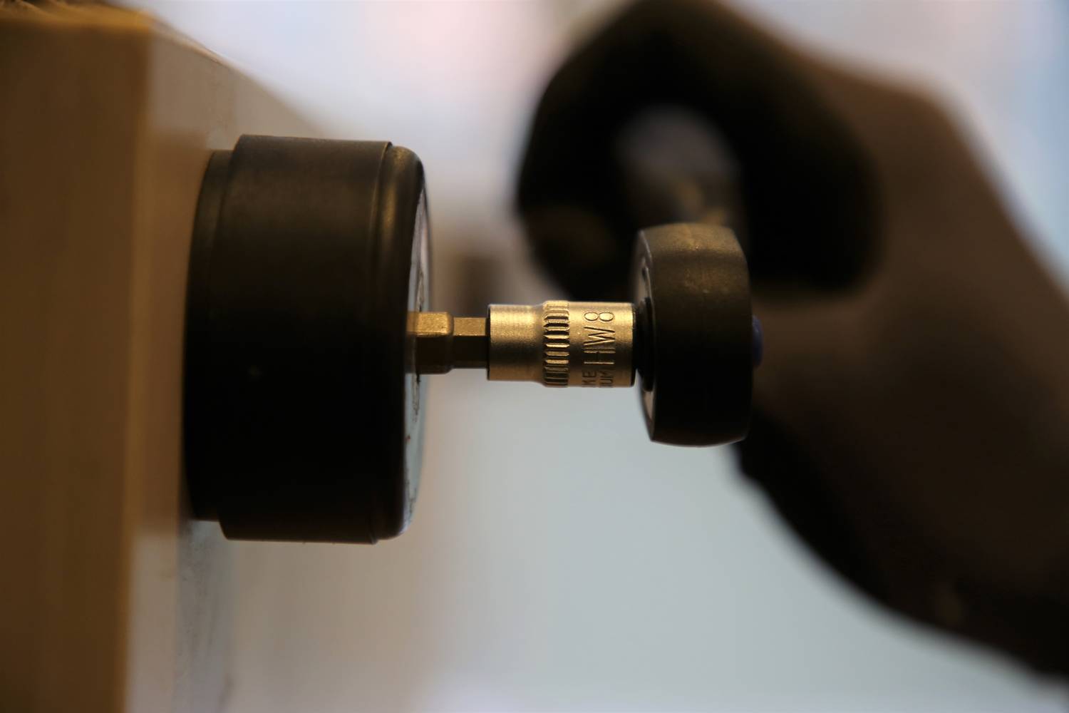 A hand wearing a black glove turns a measuring instrument. The focus is on the tool and the action.