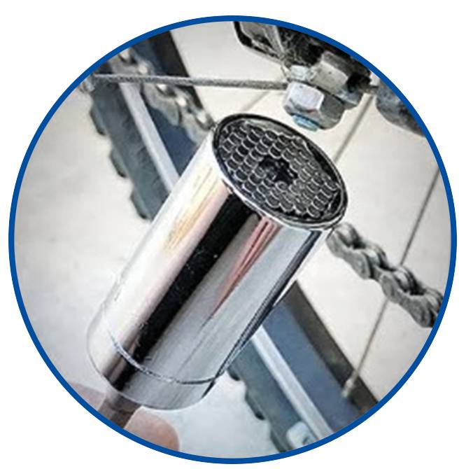 A universal wheel spanner is being used on a wheel bolt. It is cylindrical, silver, and has a honeycomb-like head. A bicycle derailleur is visible in the background.