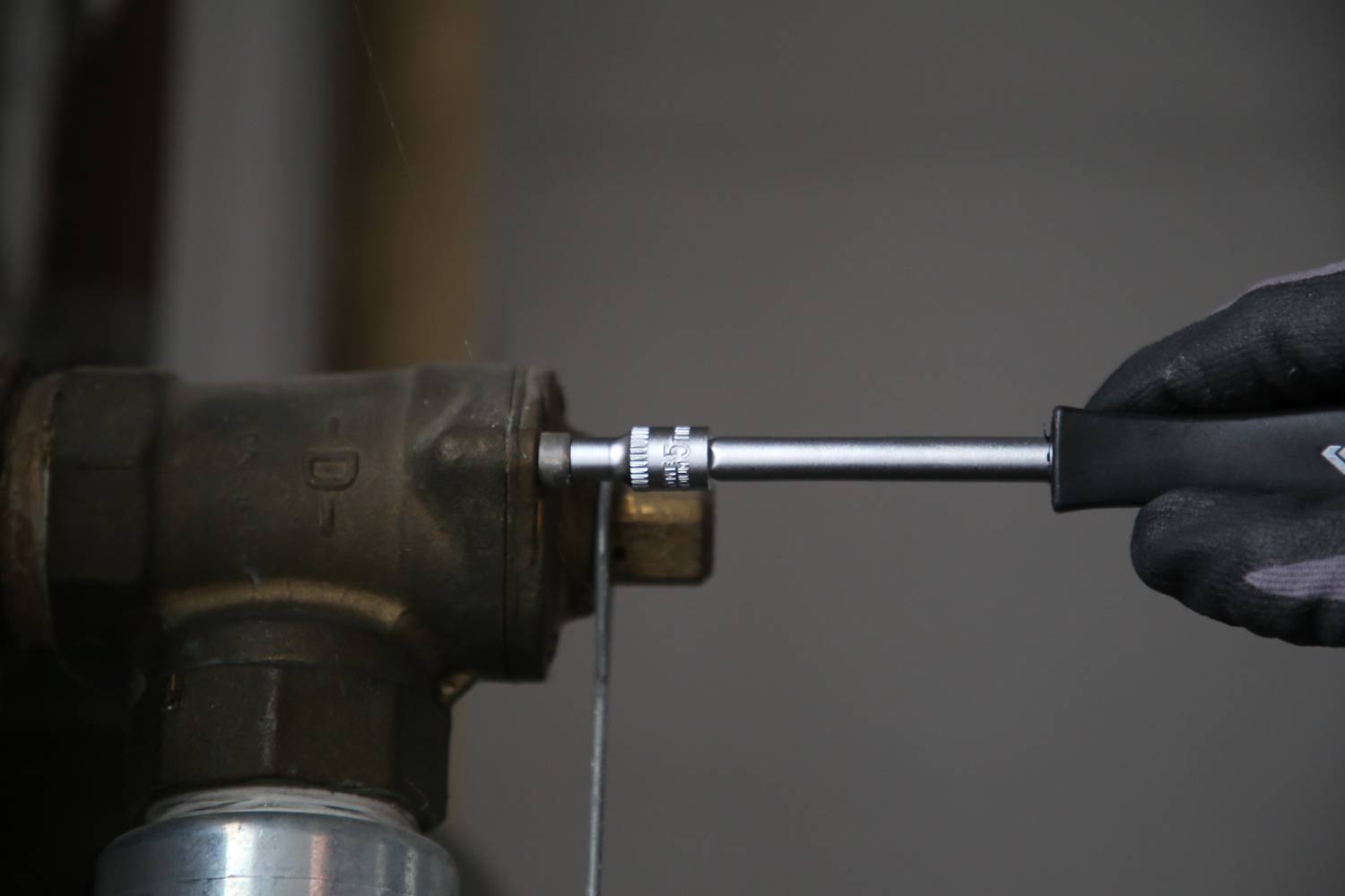 A person is tightening a screw on a metal pipe with a spanner.