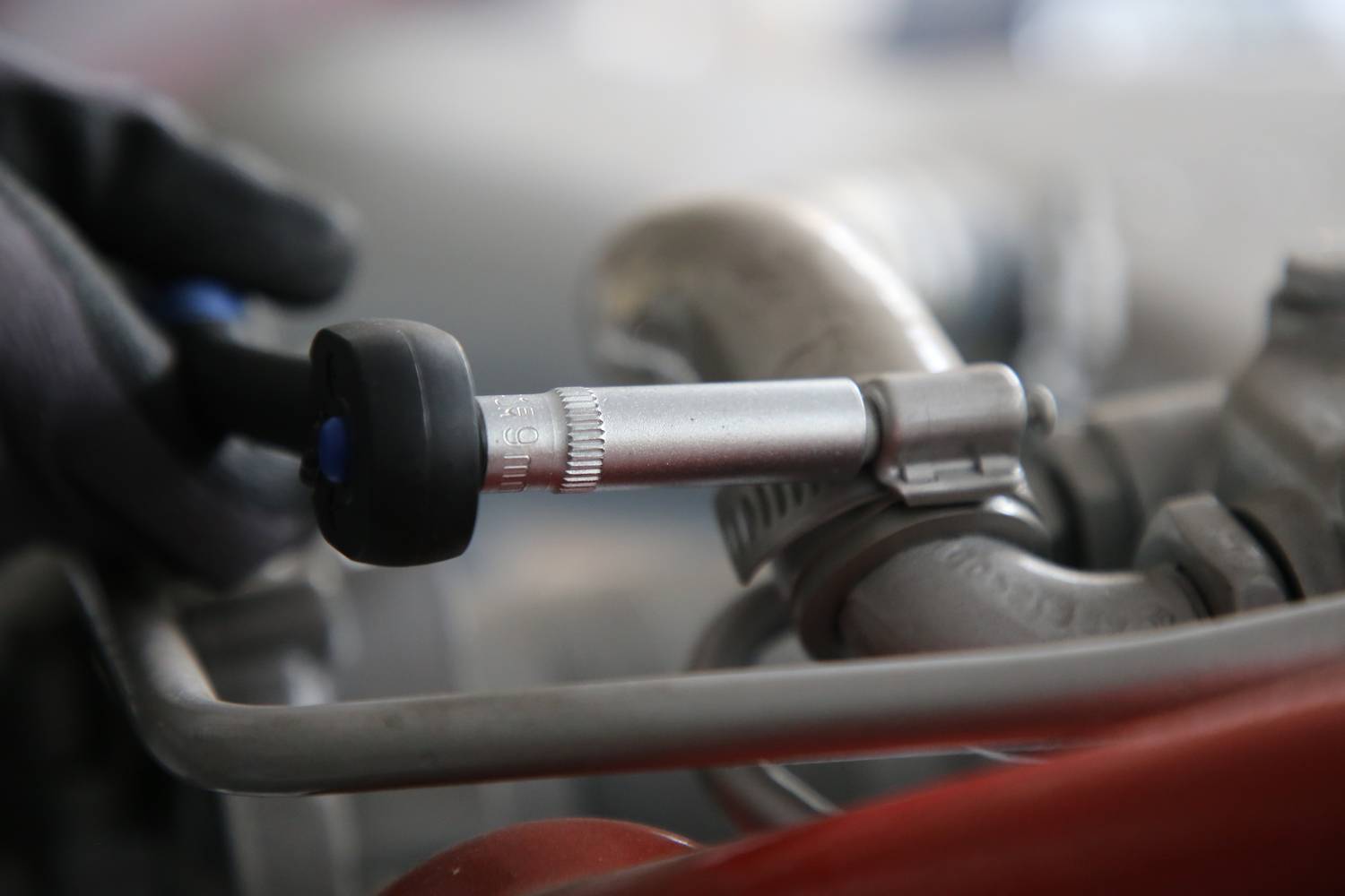 A person is measuring the tyre pressure with a pressure gauge on a car tyre. The focus is on the tyre valve and the measuring device.