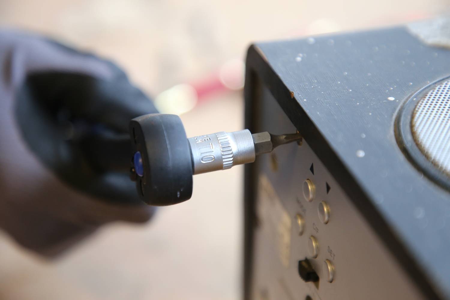 A person wearing gloves is tightening a screw on an electronic device with a tool.