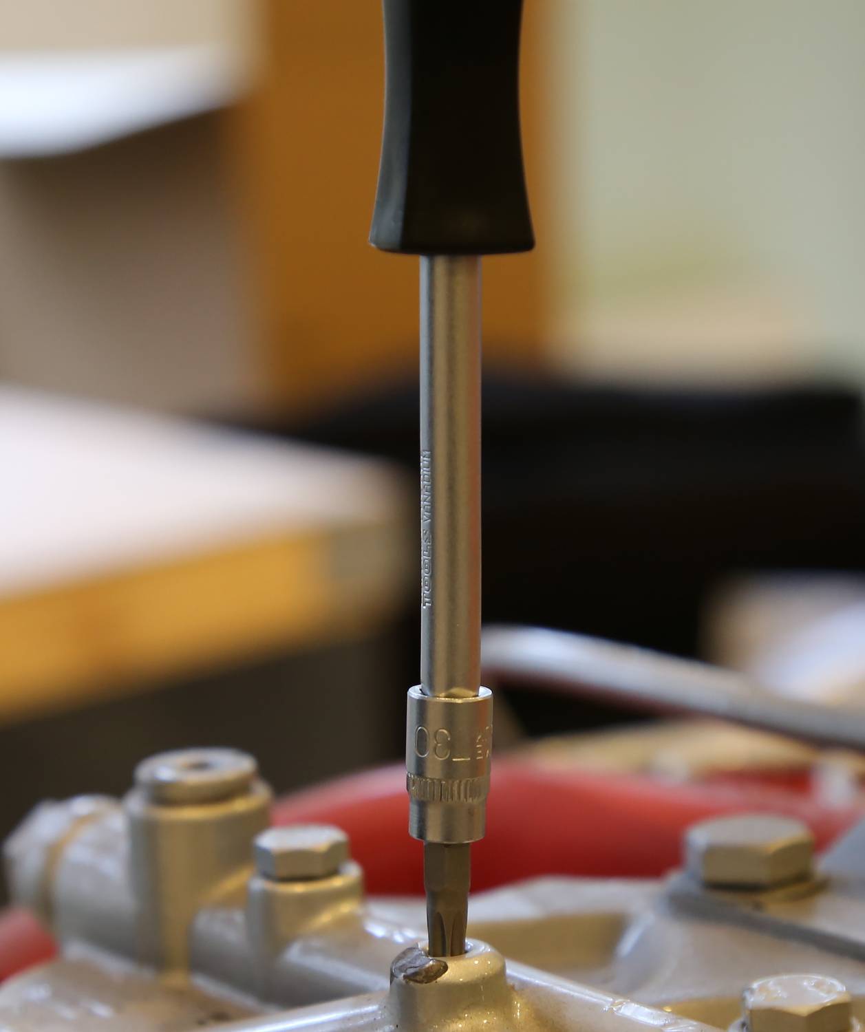 A screwdriver with a black handle is used to secure a screw to a metal surface.