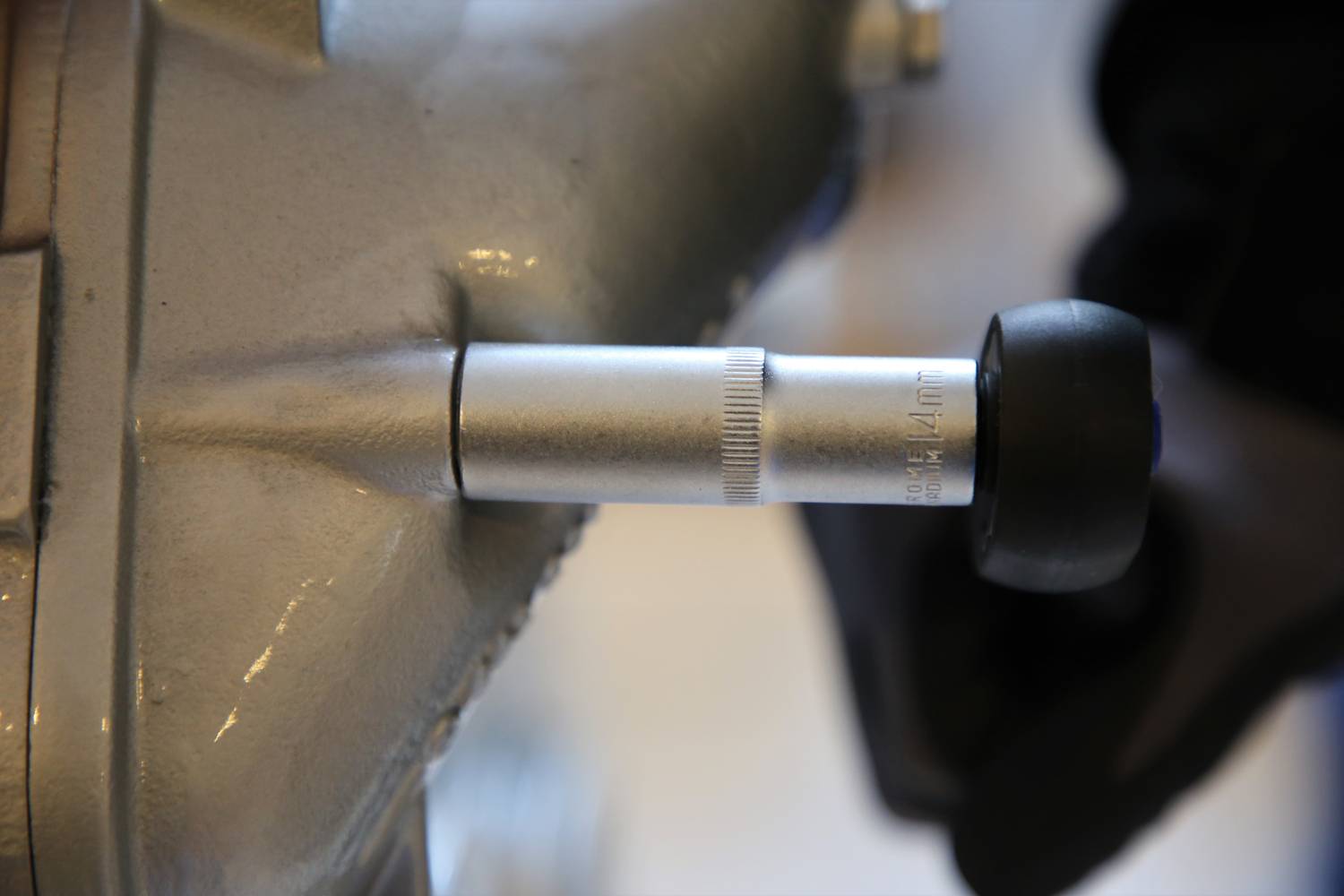 A silver torque tool is being applied by a person wearing a black glove to a metal component, presumably for adjustment.