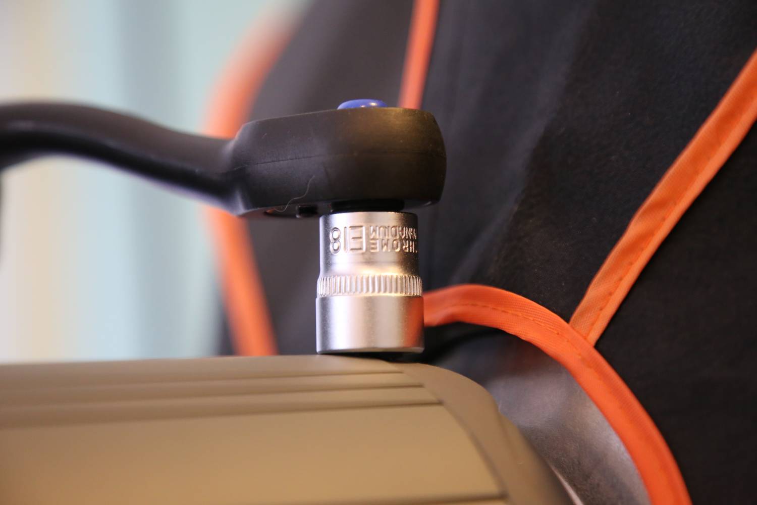 Close-up of a torque wrench positioned on a screw, against an orange-black background.