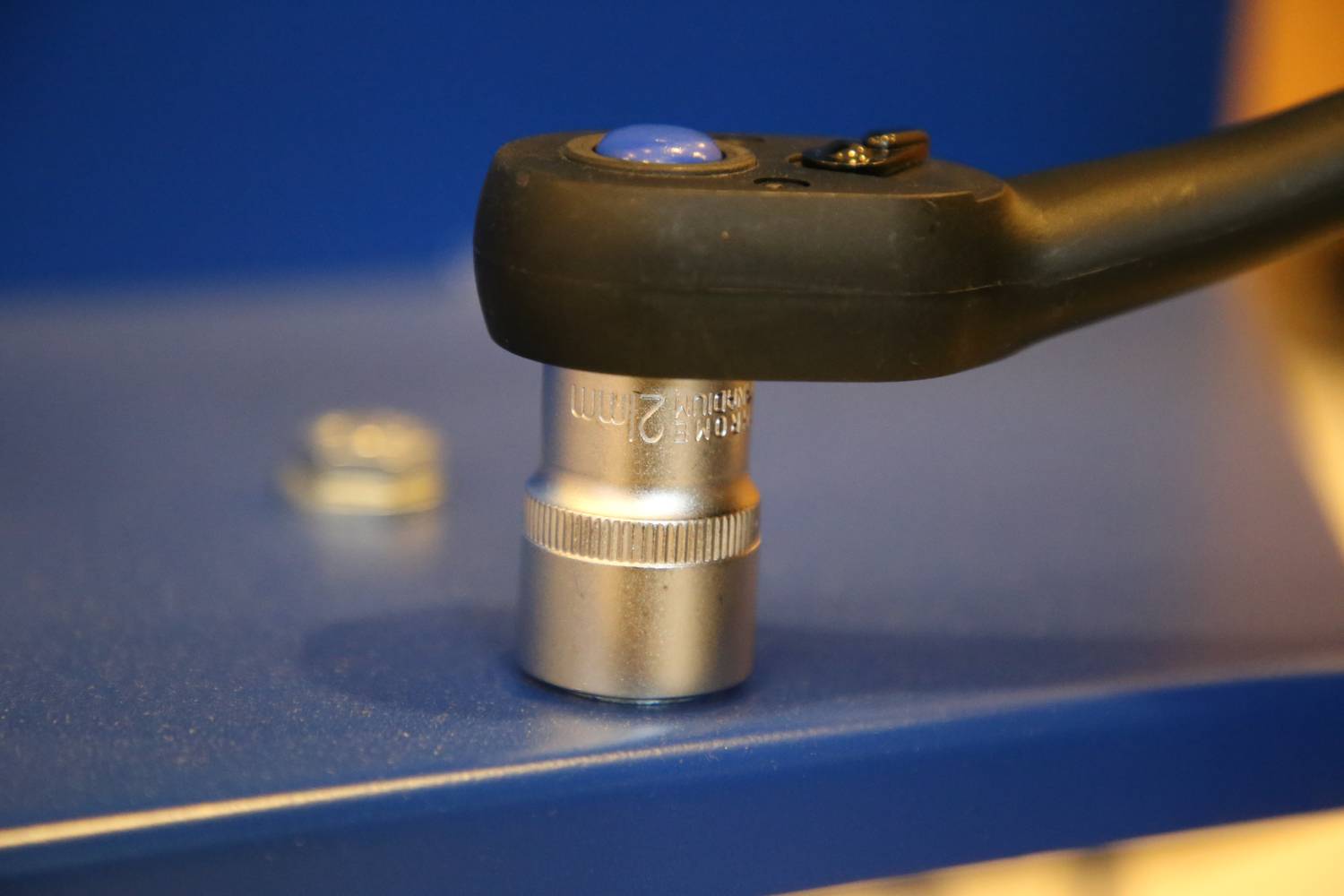 A 22mm socket spanner is laid on a blue surface. Another screw is visible in the background.