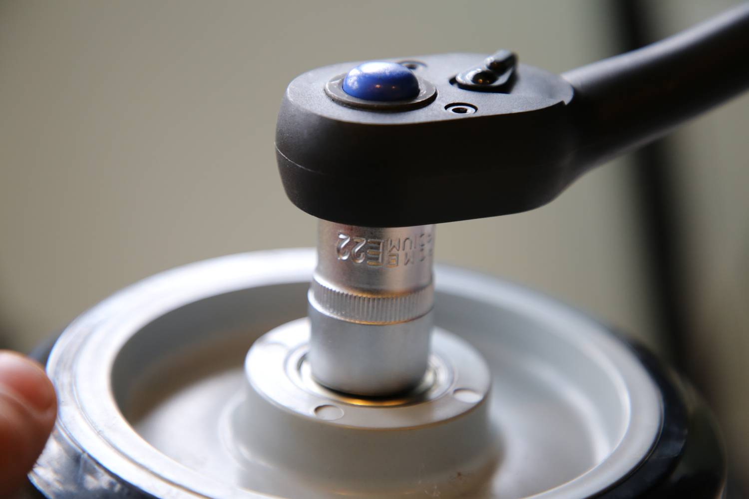 A ratchet with a socket is positioned on a nut of a cylindrical component, ready to tighten or loosen.