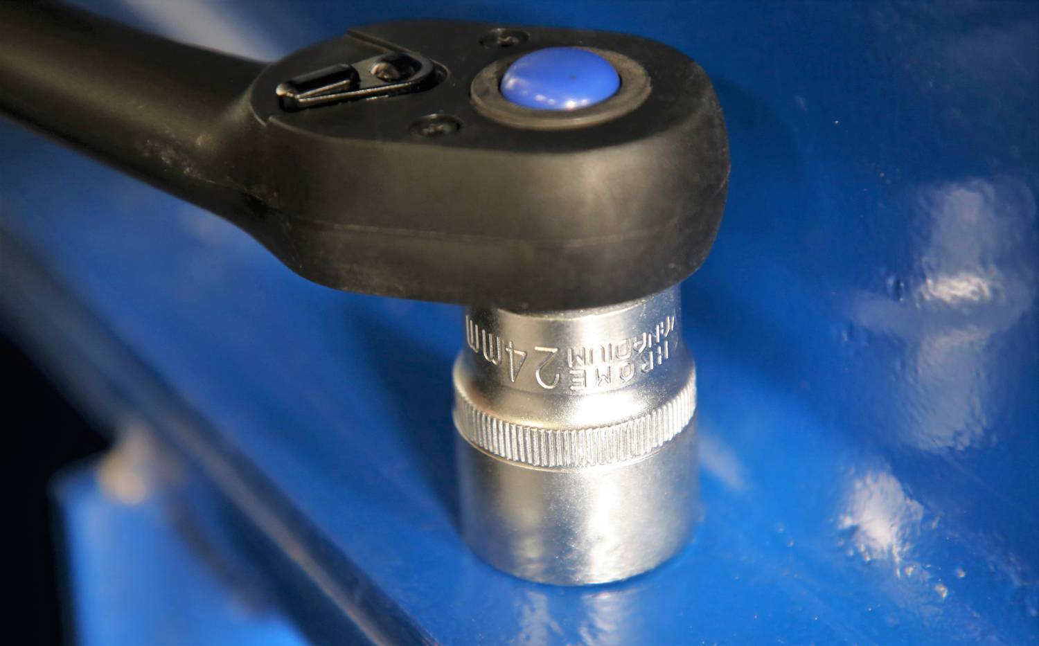 A ratchet with a black handle and blue button is gripping a 21-mm socket, which is secured on a blue surface.